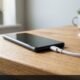 Smartphone connected to charging cable on oak desk while battery drains