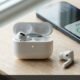 Open AirPods charging case with amber LED on desk with one earbud charging and one dead on table